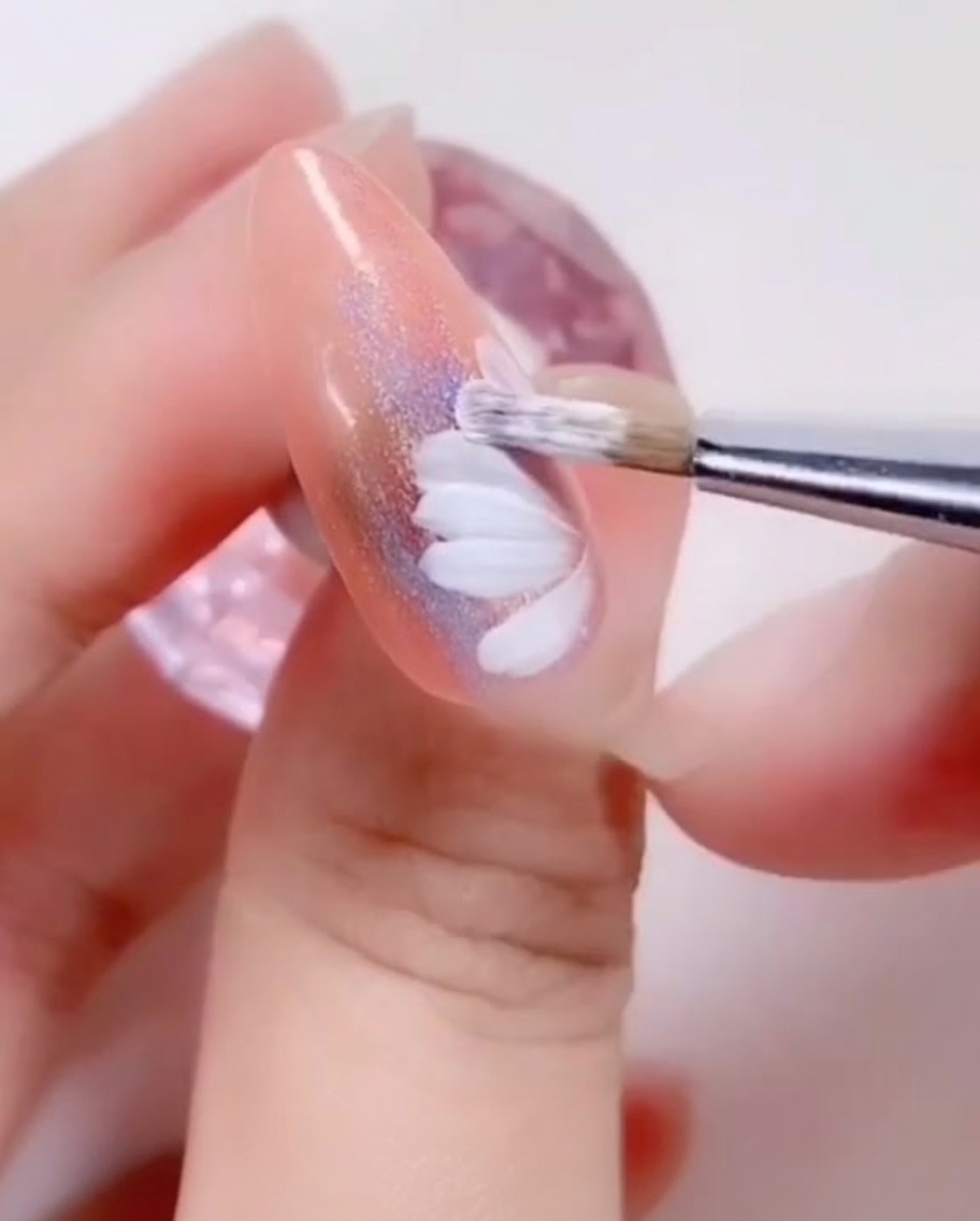 A close-up of a nail brush painting small white petals onto the inner center of a daisy design.