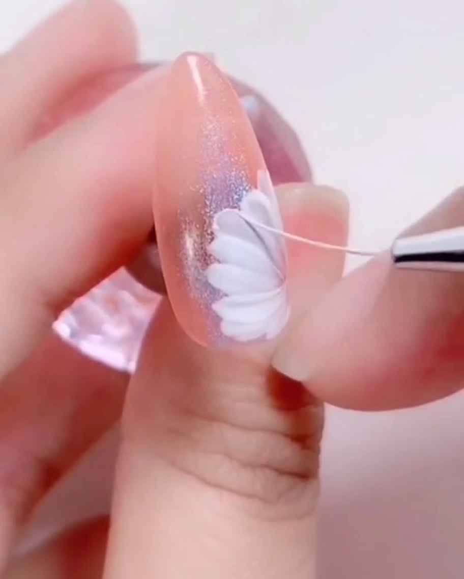 A fine-tipped brush placing a small, dark center dot onto the middle of the painted white daisy.