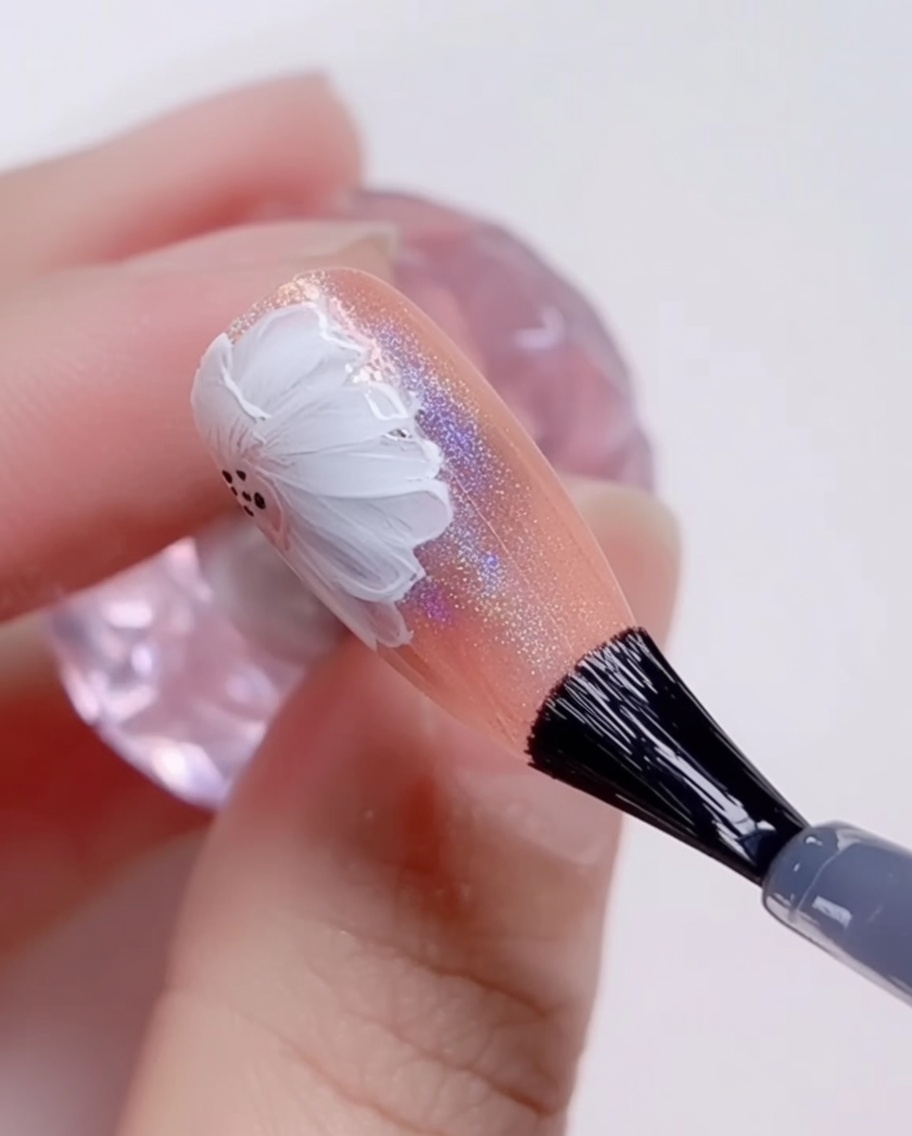 A brush applying a final, clear, glossy top coat over a finished daisy nail art design.