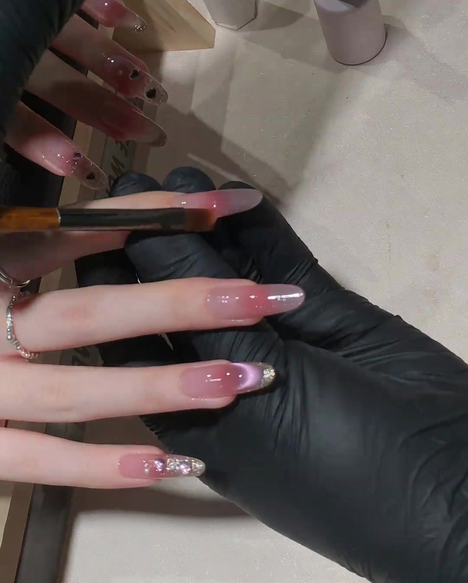 A small flat brush being used to feather the pink gel upward on the nail for a gradient effect.