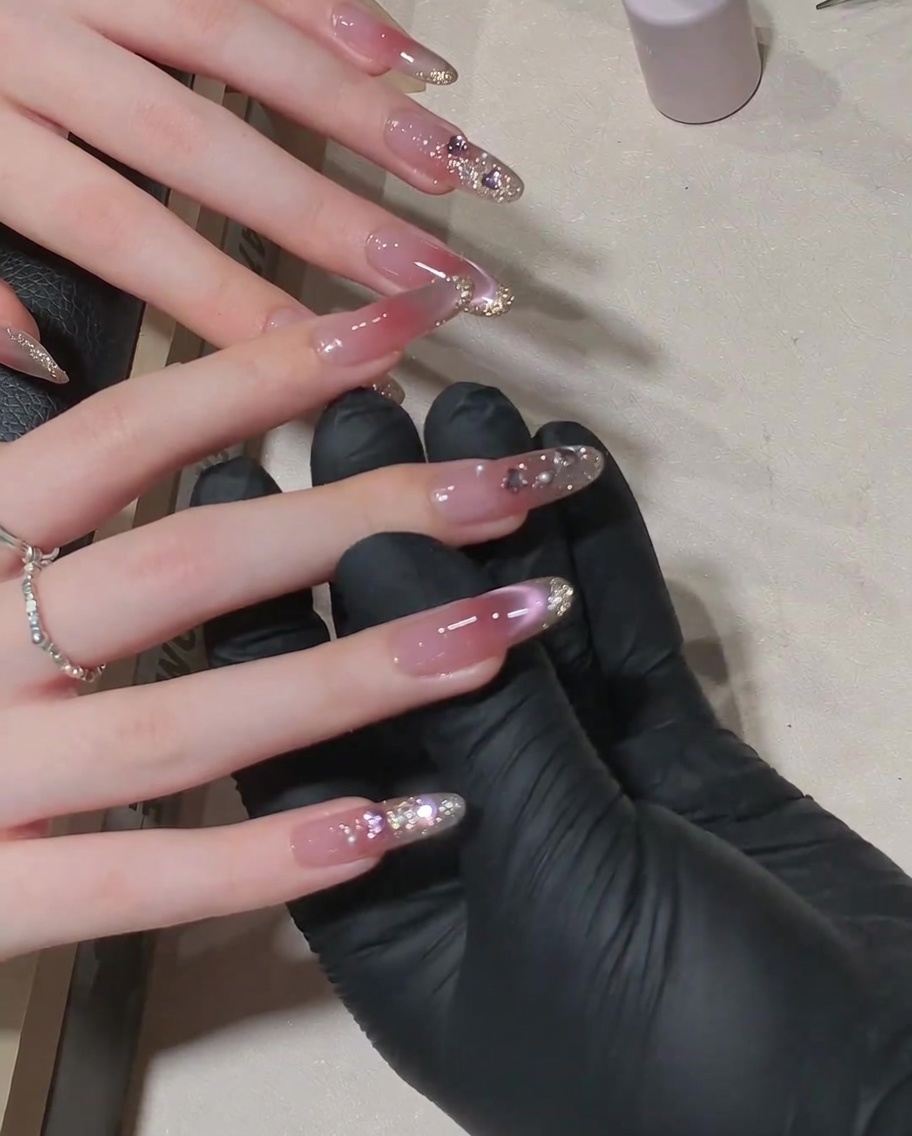 A brush applying a final glossy top coat over a finished nail design with rhinestones.