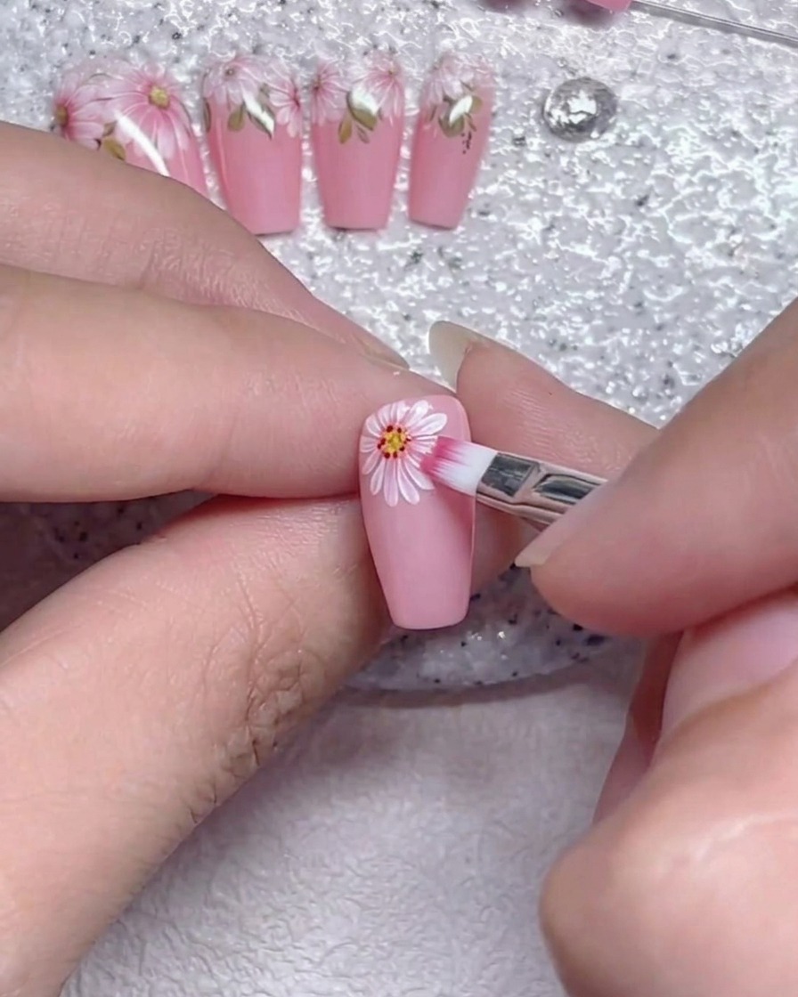 A flat brush gently blending the edges of white flower petals on a pink nail.