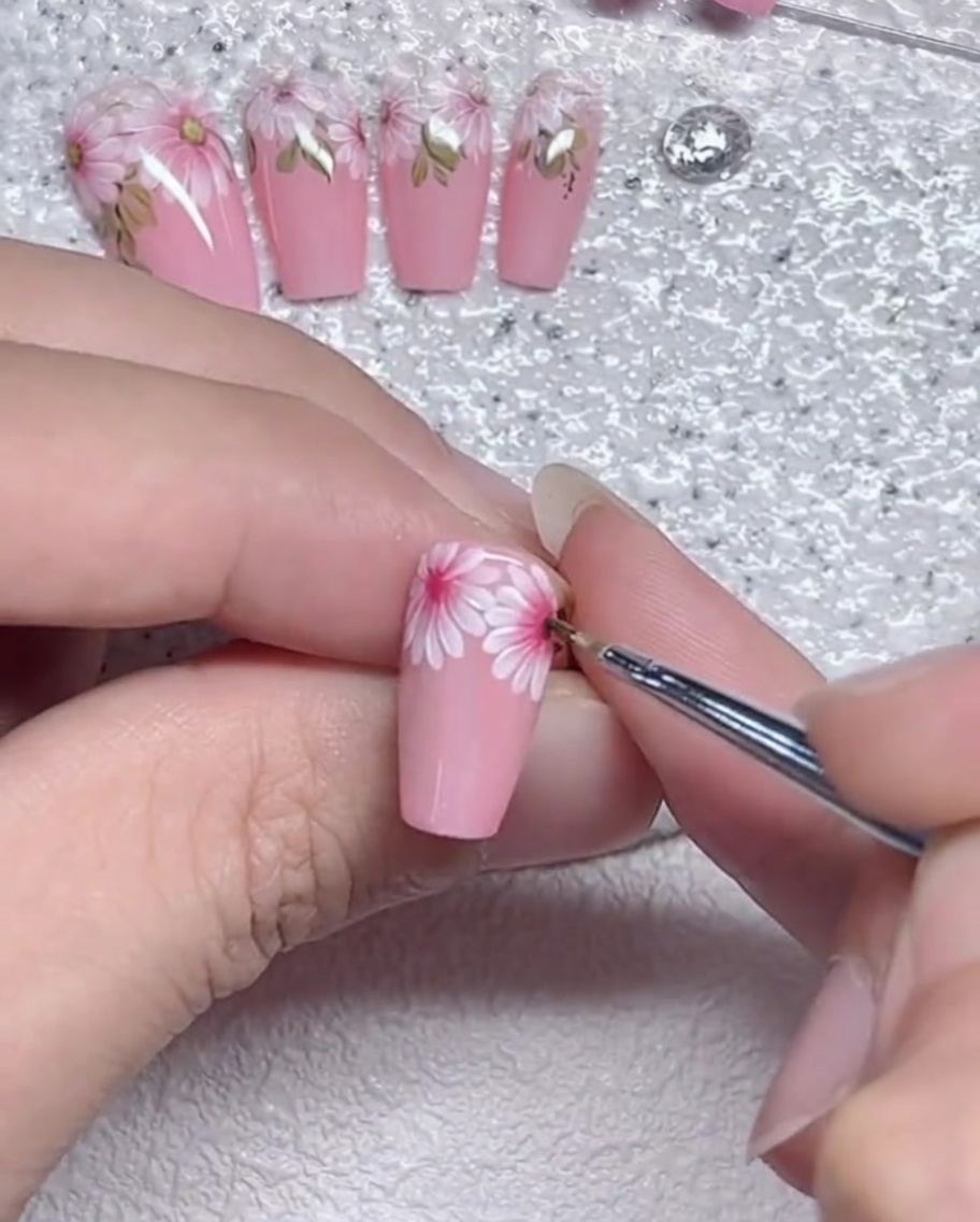 A close-up view of a fine liner brush refining the edges of daisy petals on a nail.