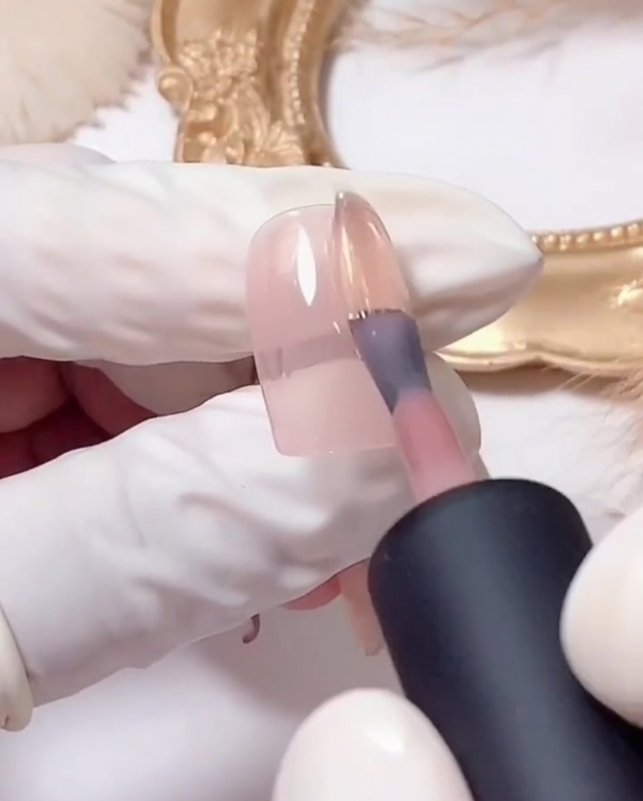 A flat brush depositing silver glitter gel onto the tip of a pink-coated nail.