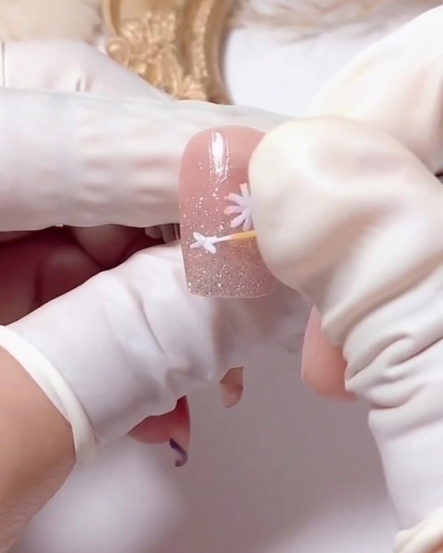 A toothpick being used to carefully separate and define the white petals of a painted daisy.