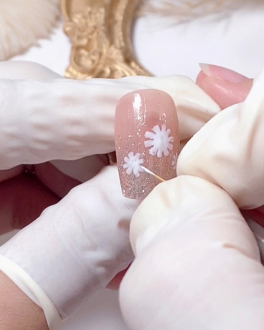 A close-up of a dotting tool touching the center of a white daisy on a nail.