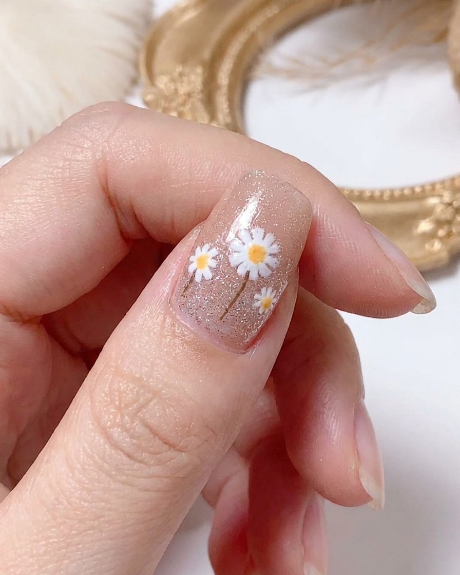 A hand curing the finished daisy nail design under a lamp.