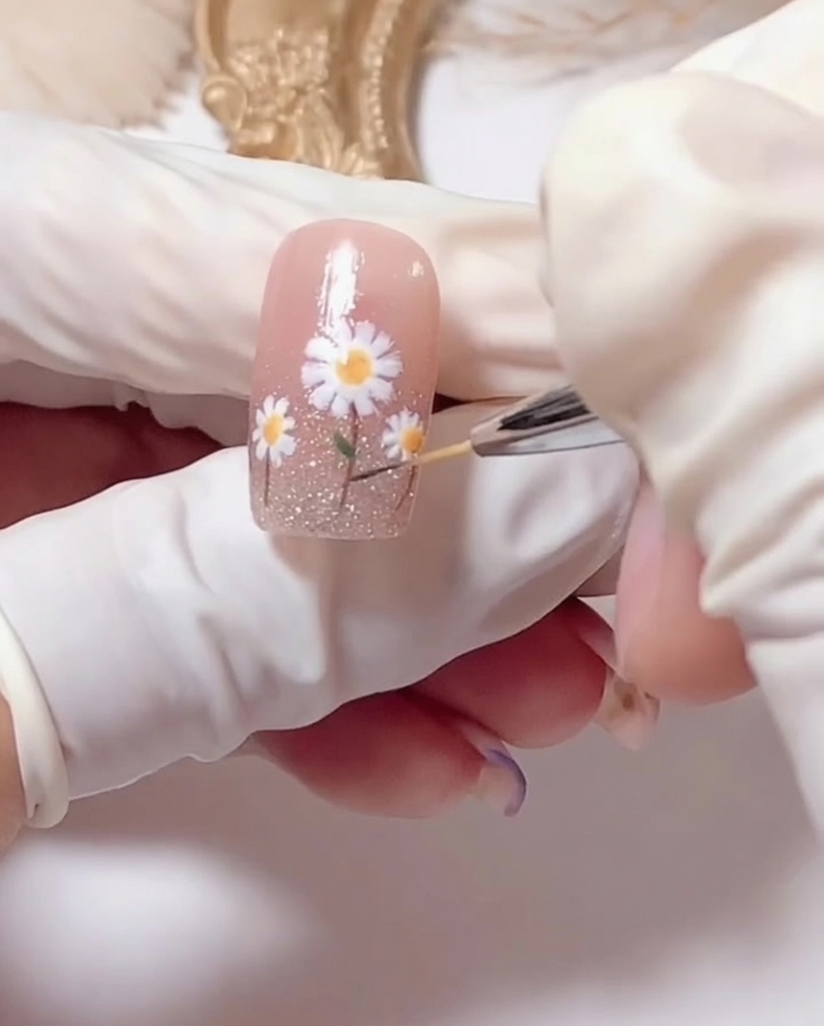 A brush applying clear glossy top coat over the finished daisy nail art.