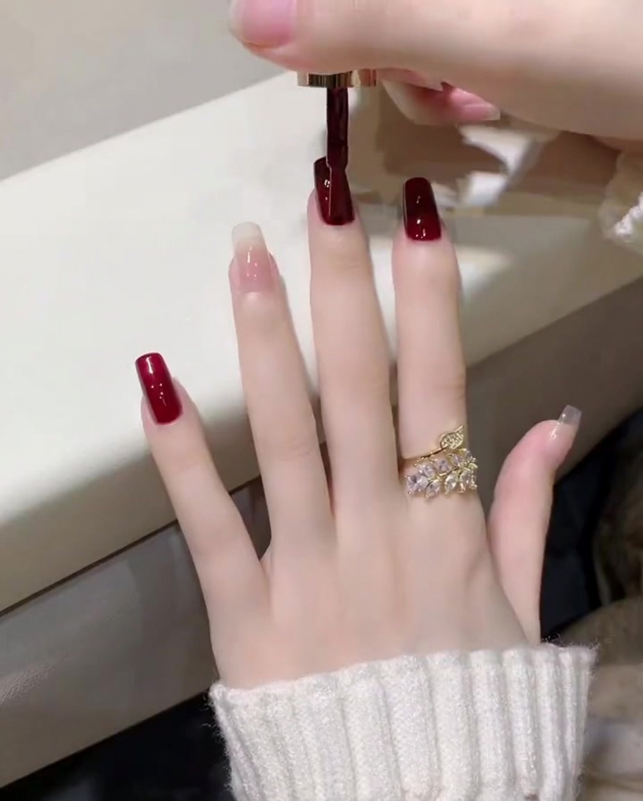 A close-up of a dark wine red gel polish being applied with a brush to a thumbnail.