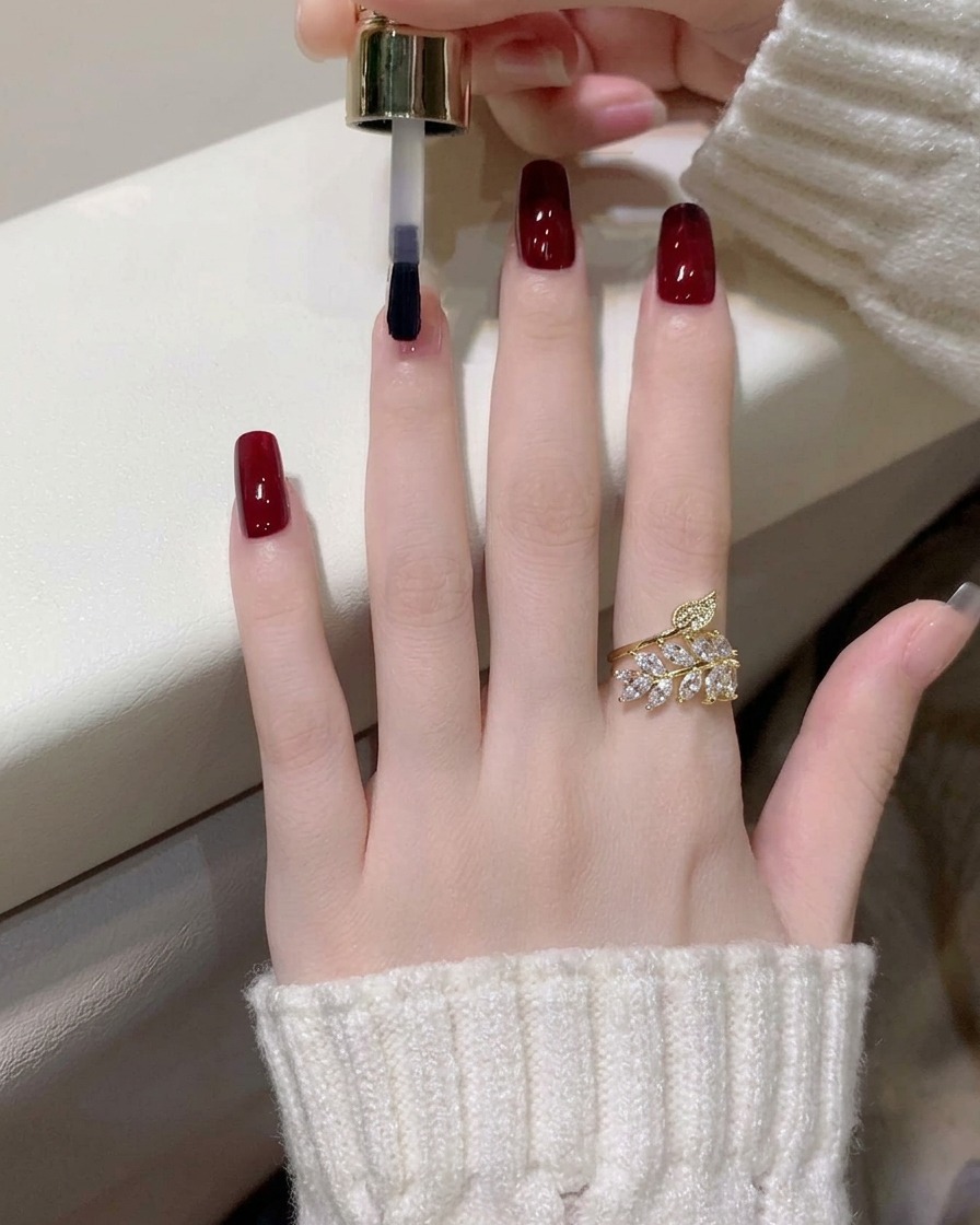 A close-up of a second coat of dark wine red gel polish being applied to the index finger.