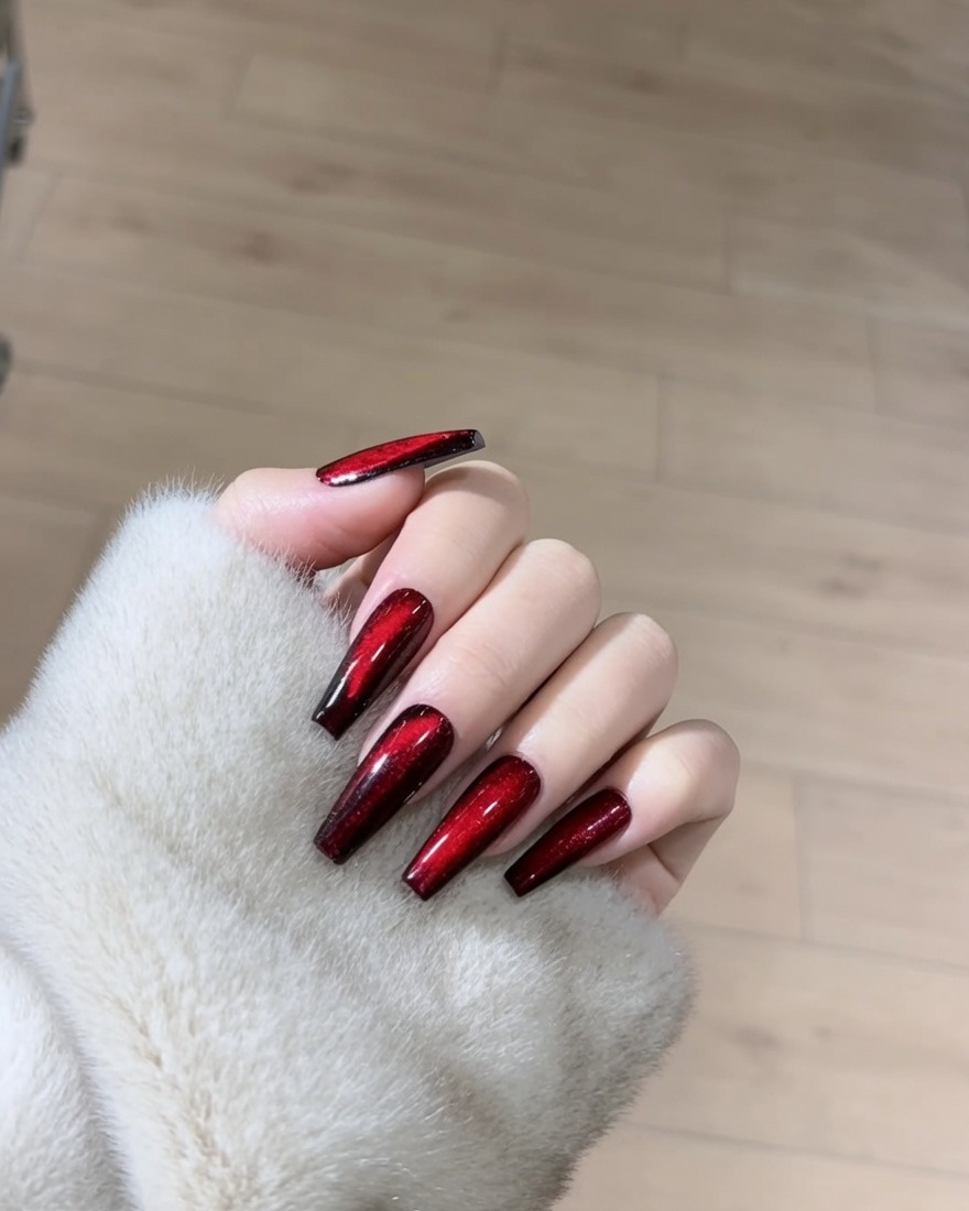 A close-up of a nail being coated with a shimmery red magnetic gel polish.