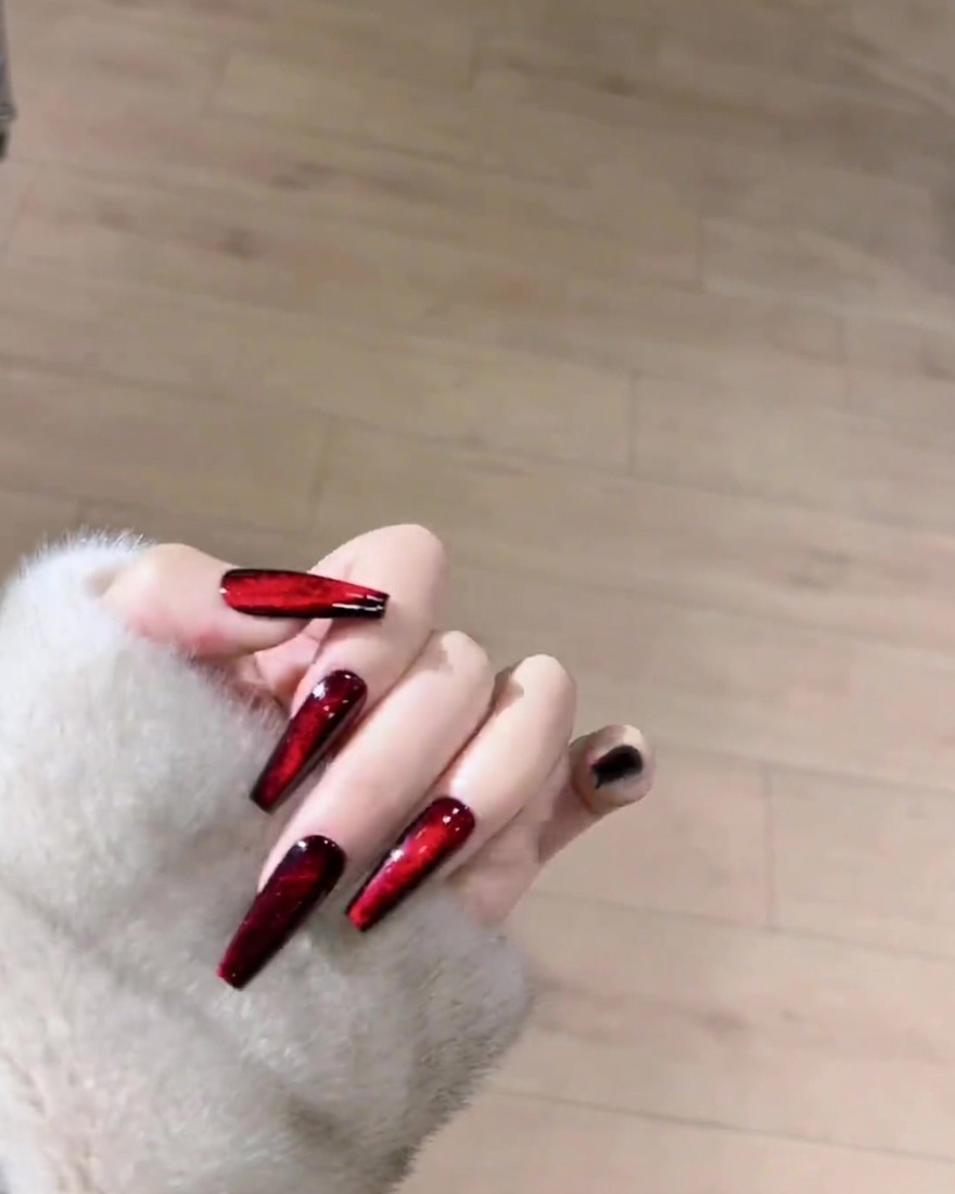 A magnet positioned over a wet, red magnetic gel-coated nail to shape the shimmer particles into a line.