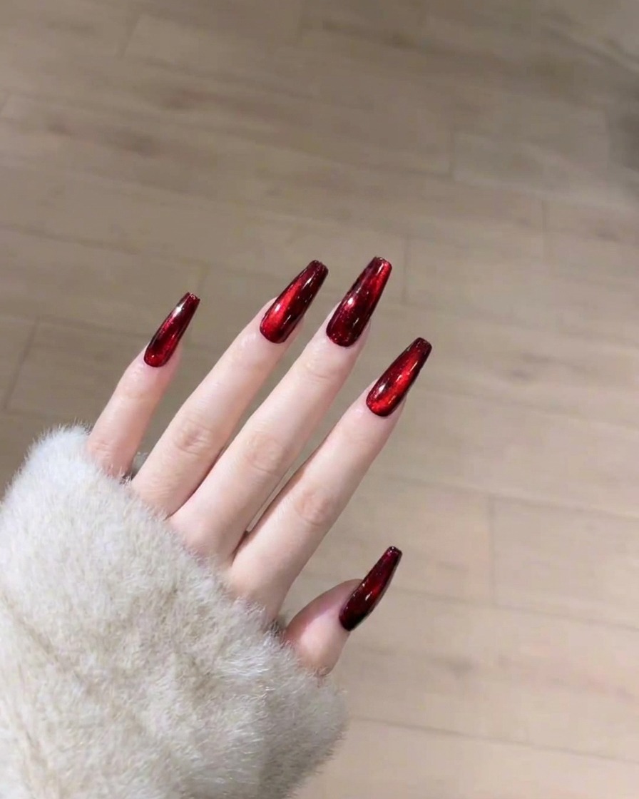 A brush applying a smooth, clear layer of glossy top coat over the cured red cat-eye nail.