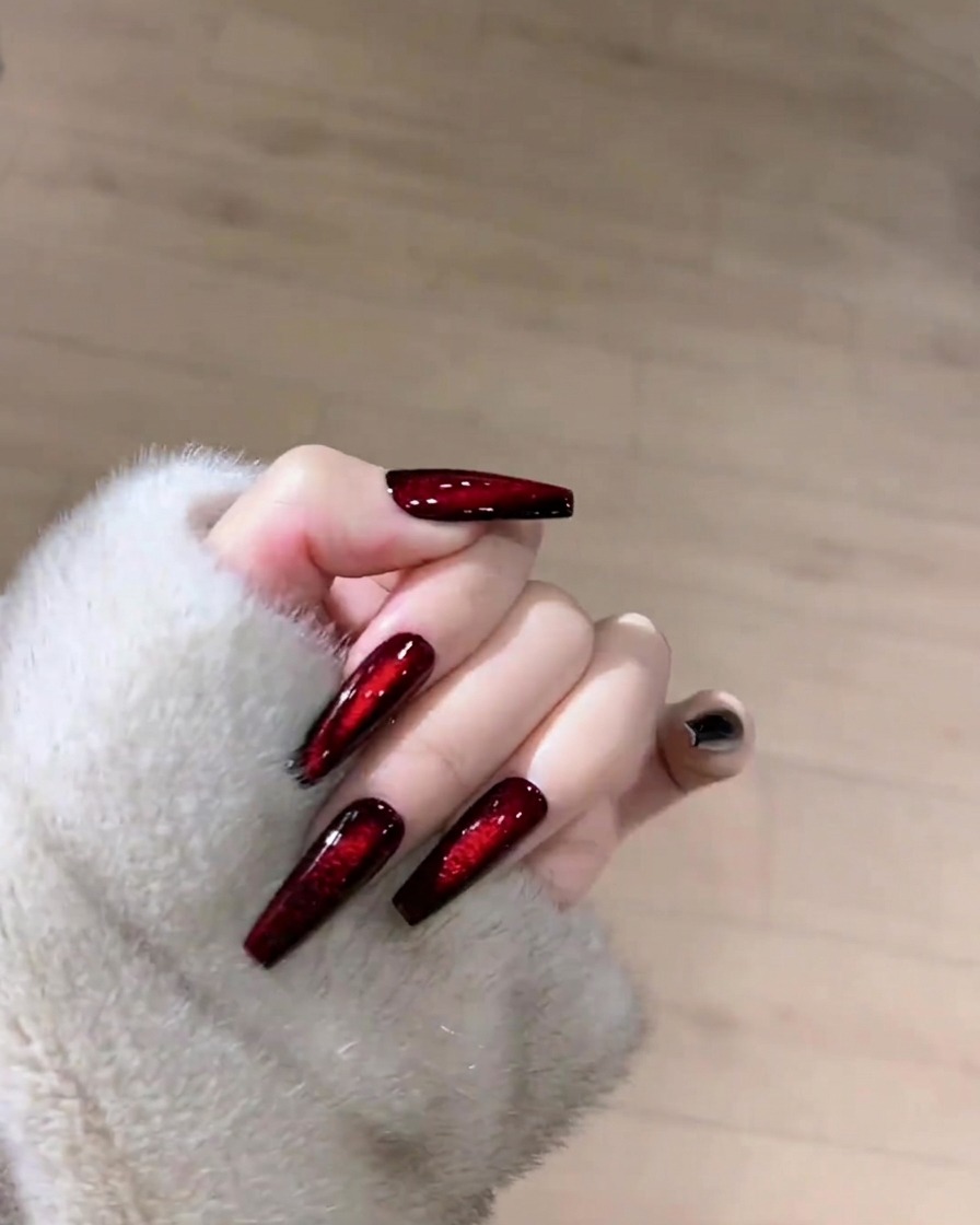 A hand holding a lint-free wipe, cleaning the surface of a dark ruby cat-eye nail.