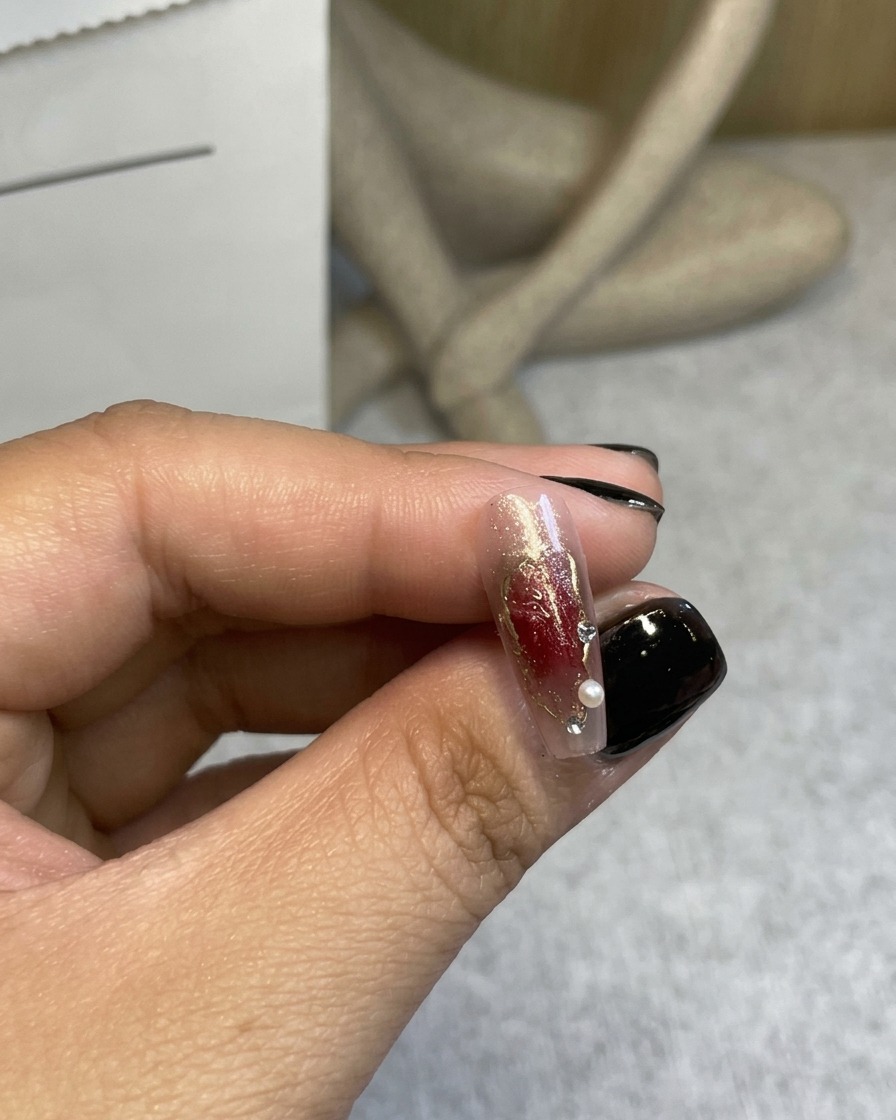 A close-up of a 3D wine-red rose being placed onto a decorated nail with tweezers.
