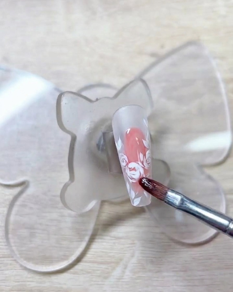 A brush applying a soft, light red gel onto the previously drawn white rose outlines.