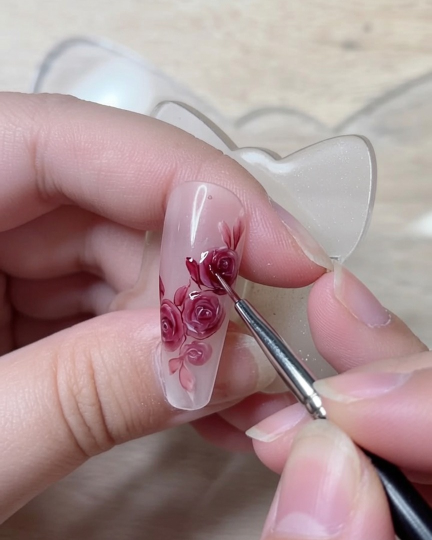 A fine detailing brush tracing crisp dark red lines to define the structural petal folds of a rose nail art design.