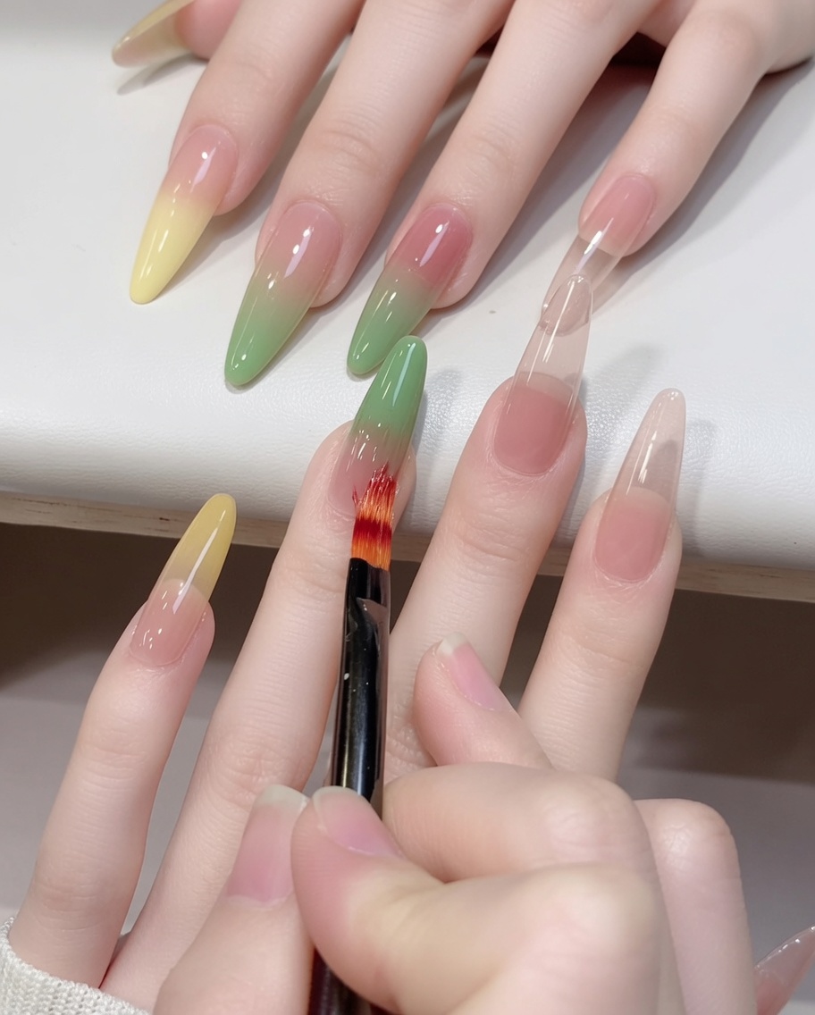 A close-up shot of an ombre brush blending green gel upwards on a nail.