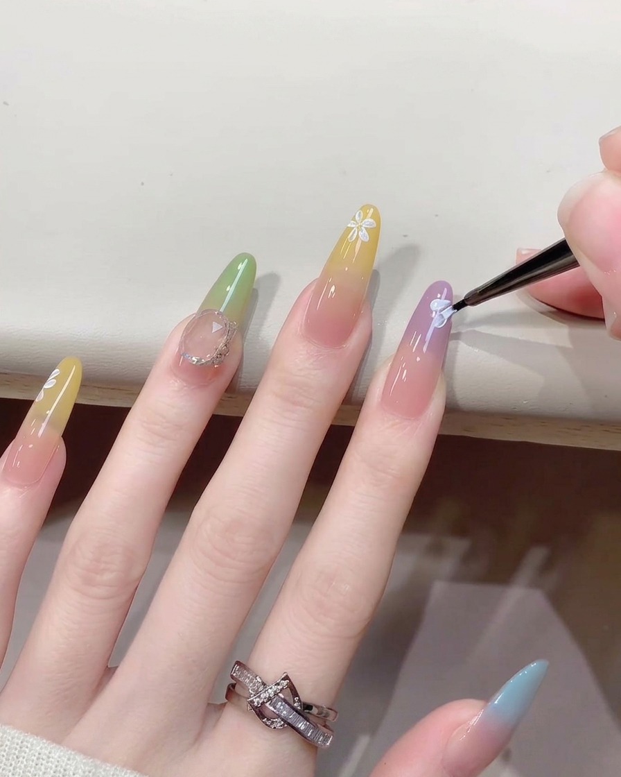 A close-up view of a fine brush adding small white center dots to a painted flower nail art design.