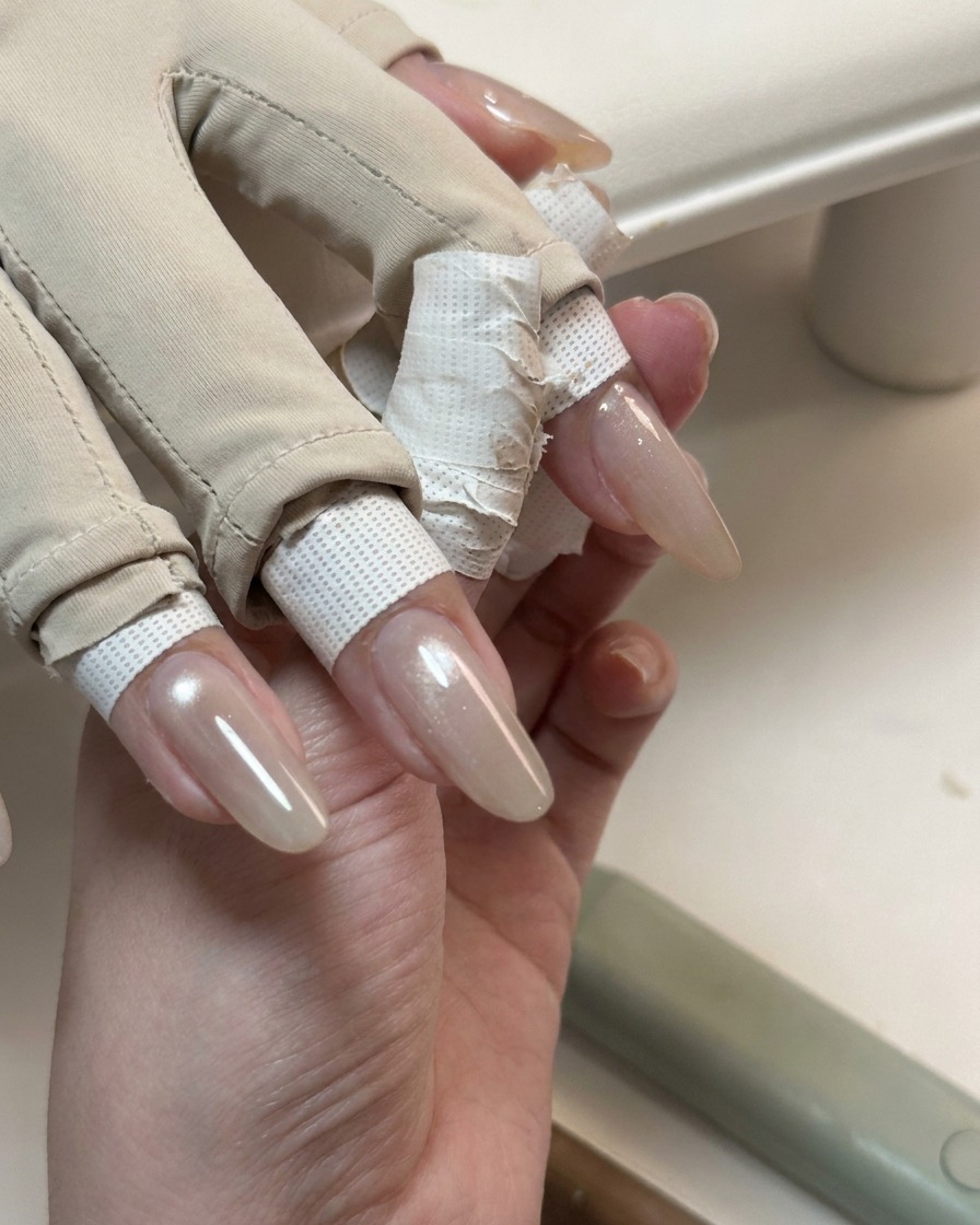 A hand showing long nails covered in a glossy, translucent cat-eye gel layer.