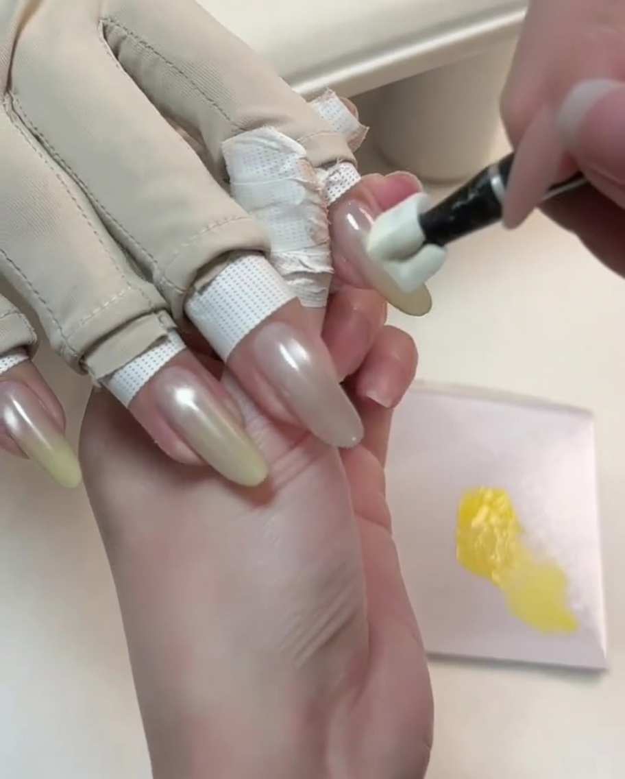 A specialized tool dabbing yellow gel onto the tip of a nude cat-eye nail to start a gradient.