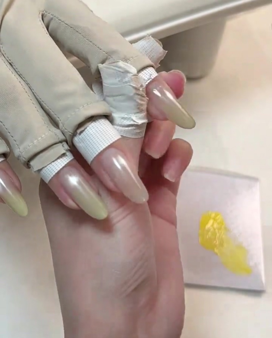A tool refining the second layer of yellow gel on the tip of a manicured nail for a brighter gradient.