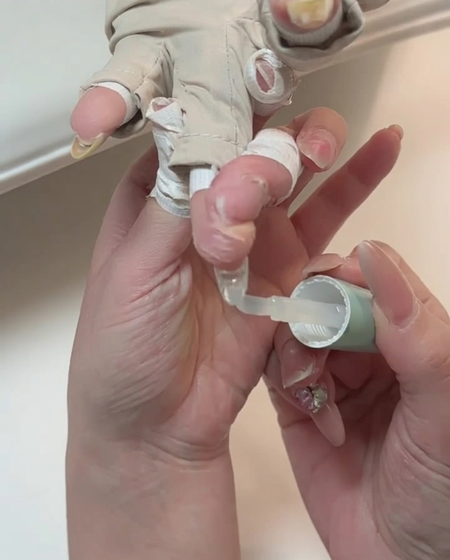 A close-up of a brush applying clear top coat to a fingernail.