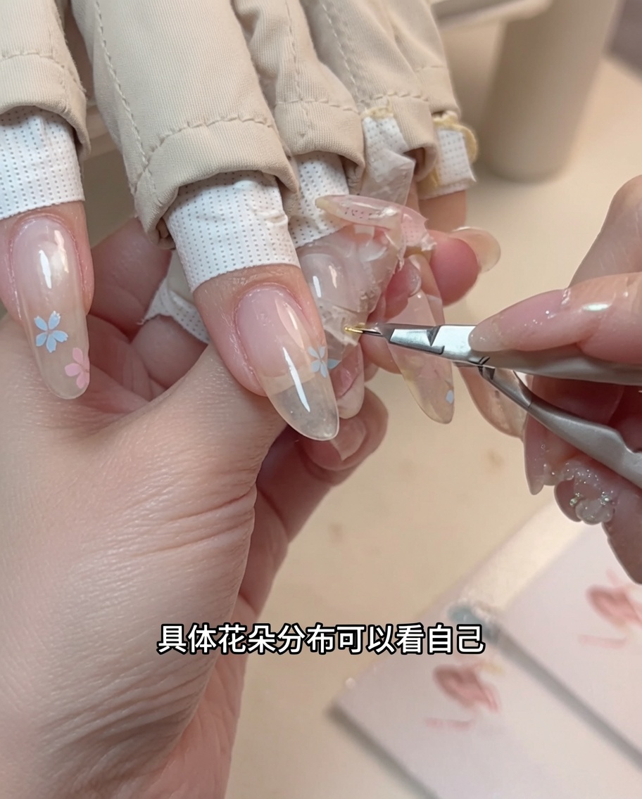 A close-up of a dotting tool applying a tiny yellow center to a painted flower on a fingernail.