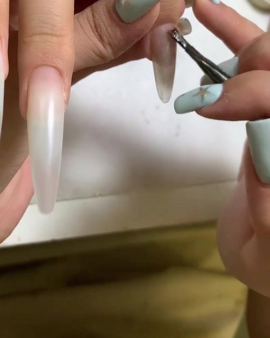 A brush applying cat eye gel polish to the surface of an acrylic nail.