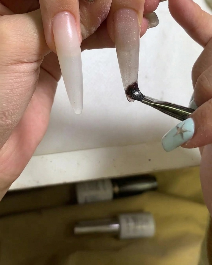 A close-up view of a brush applying cat eye gel polish onto the nail.