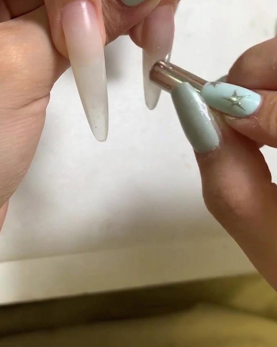 A small magnetic wand shaping the light reflection on a gel-coated fingernail.