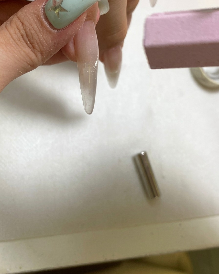A small handheld UV lamp curing a freshly magnetized gel nail.
