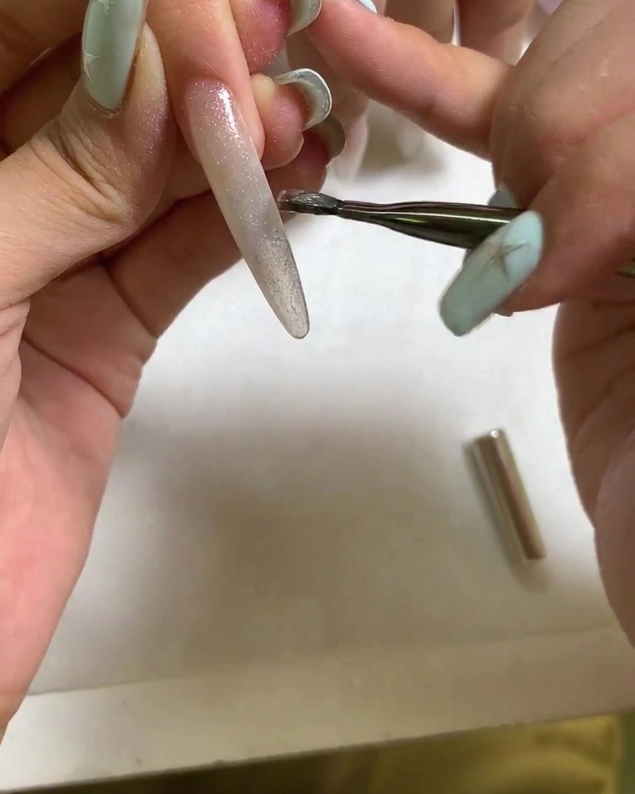 A magnetic tool held near the surface of a wet cat eye gel nail to form a bright, concentrated light reflection.
