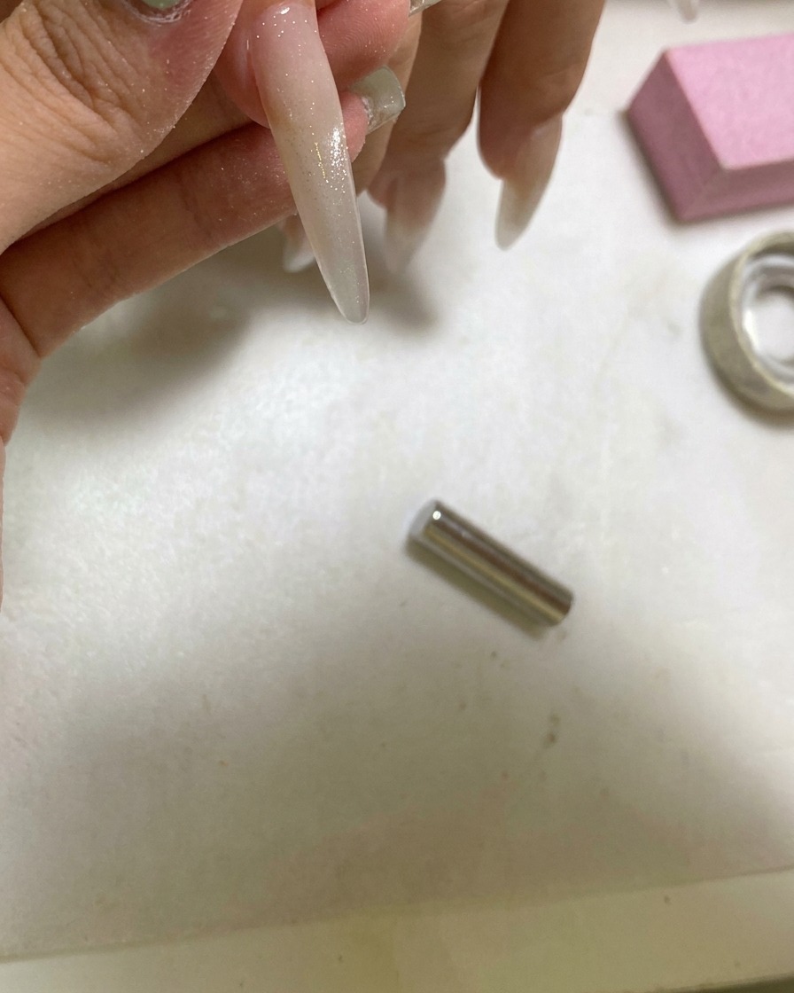 A handheld UV lamp curing a nail that has been styled with a cat eye glass ball effect.