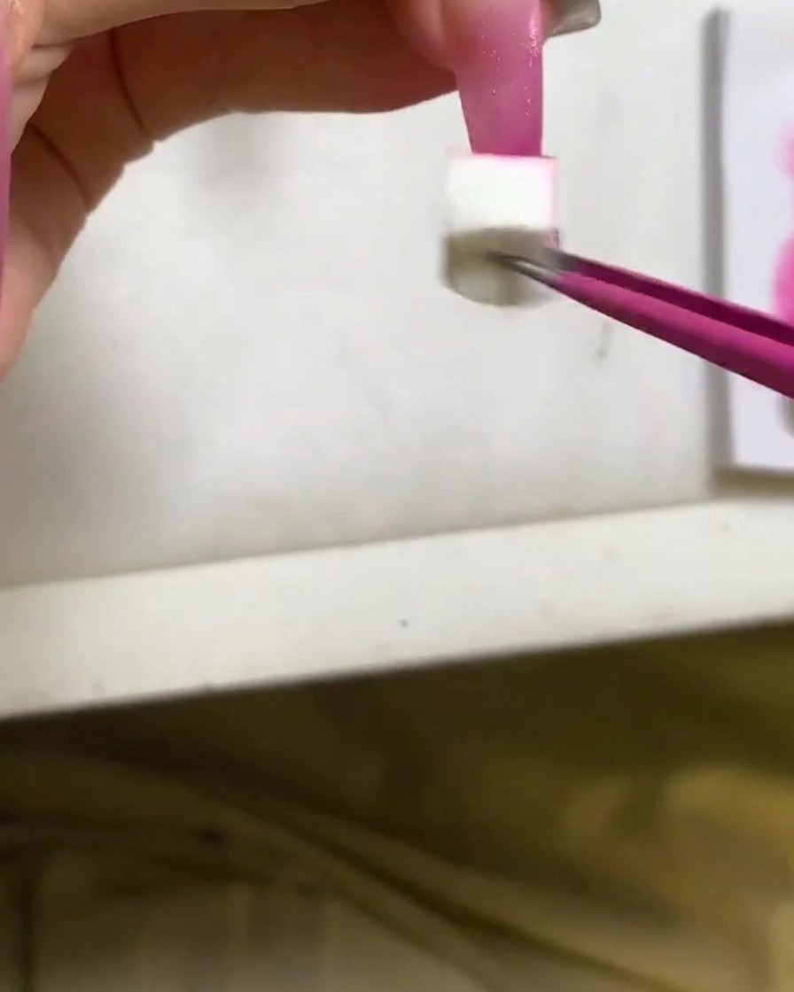A sponge applicator dabbing deep rose red gel polish onto the tip of a long nail.