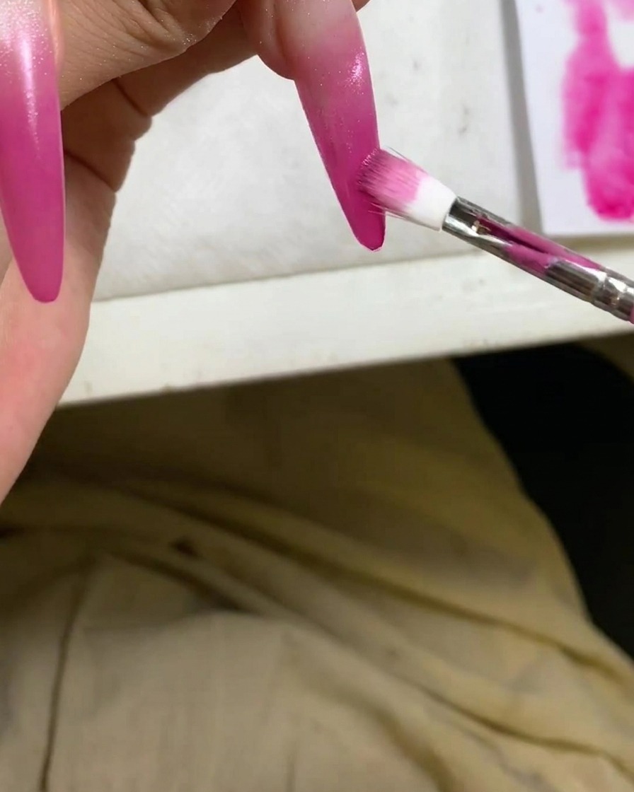 A detailed view of a sponge applicator deepening the red ombre gradient on a nail tip.