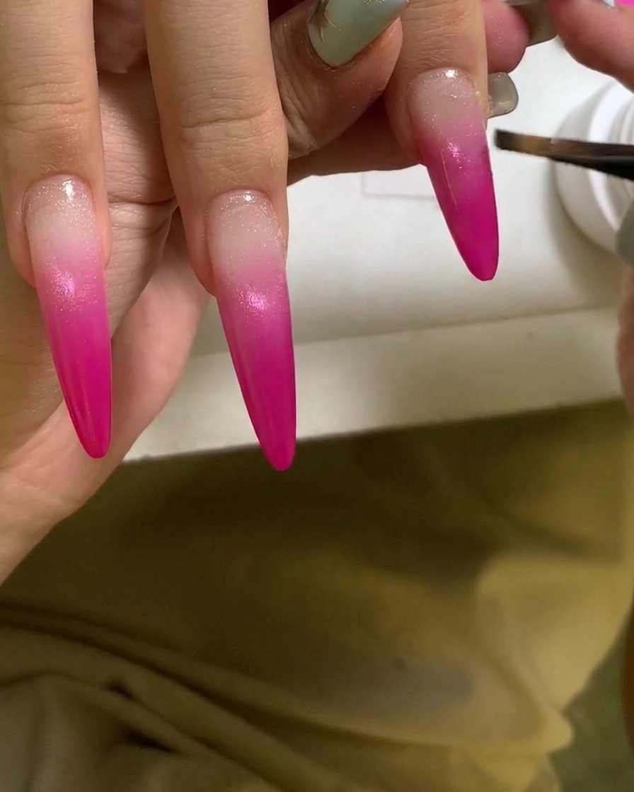 A brush applying a clear, glossy gel layer over a vibrant pink gradient nail.