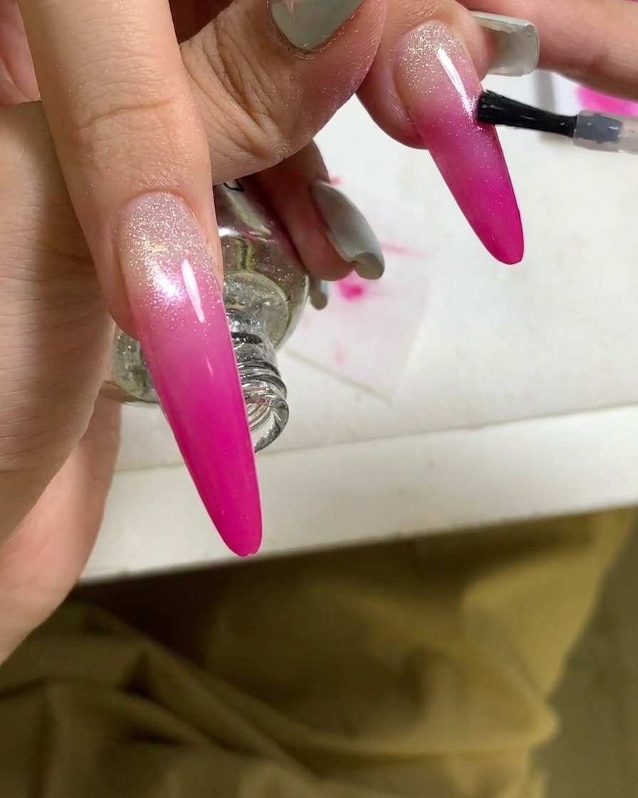 A close-up view of a brush applying a top coat to a finished pink gradient nail.