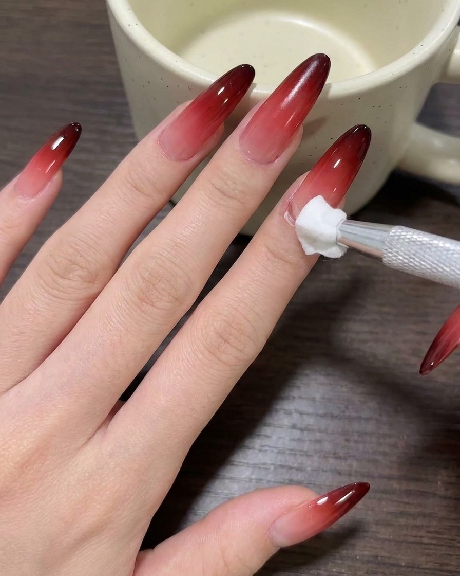 A close-up of a brush applying nude milk tea gel polish to a clean nail.