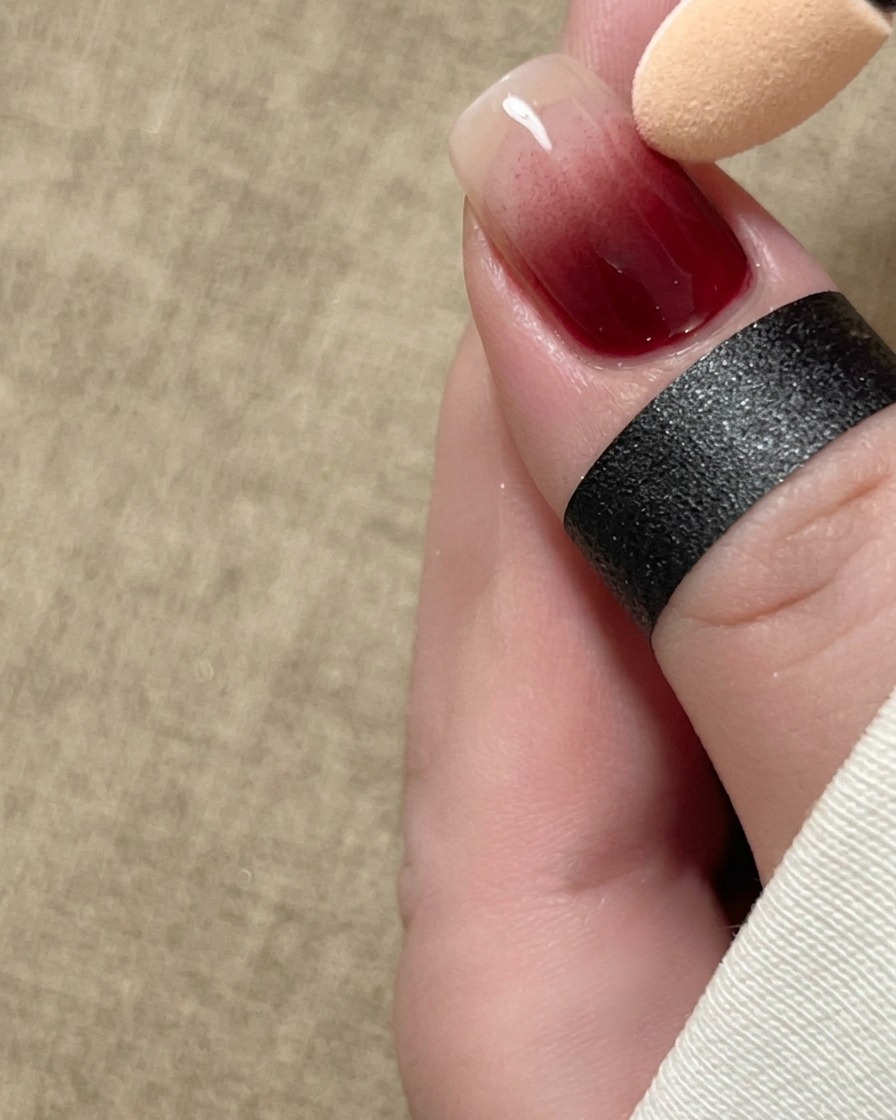 A sponge applicator softly blending red pigment in an ombre gradient down the length of a fingernail.