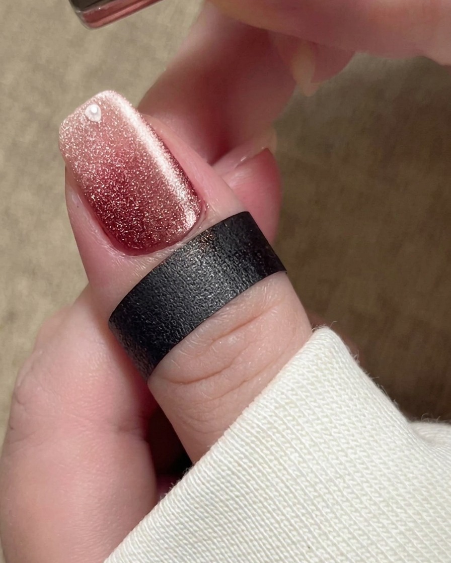 A magnet held near the nail, causing the magnetic particles in the beige polish to shift into a bright, wide shimmer band.
