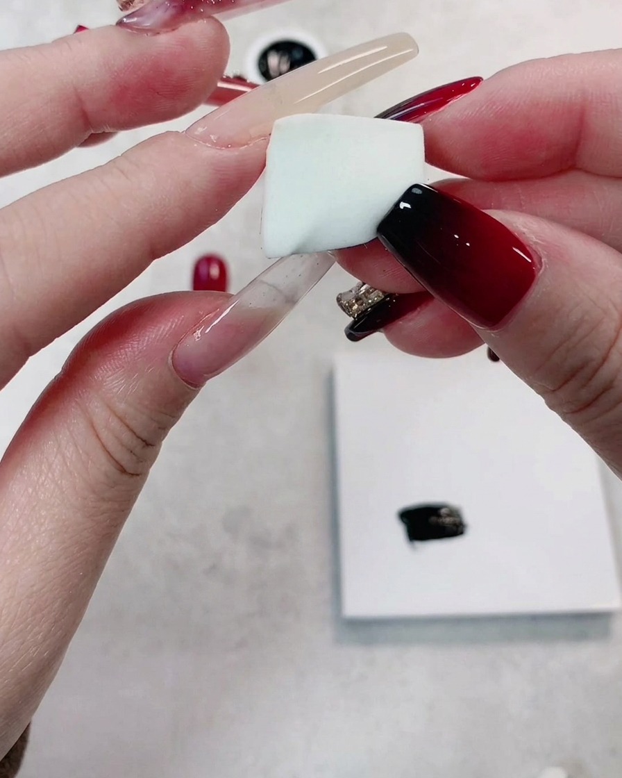 A hand holding a small, clean piece of high-density, fine-pored white sponge.