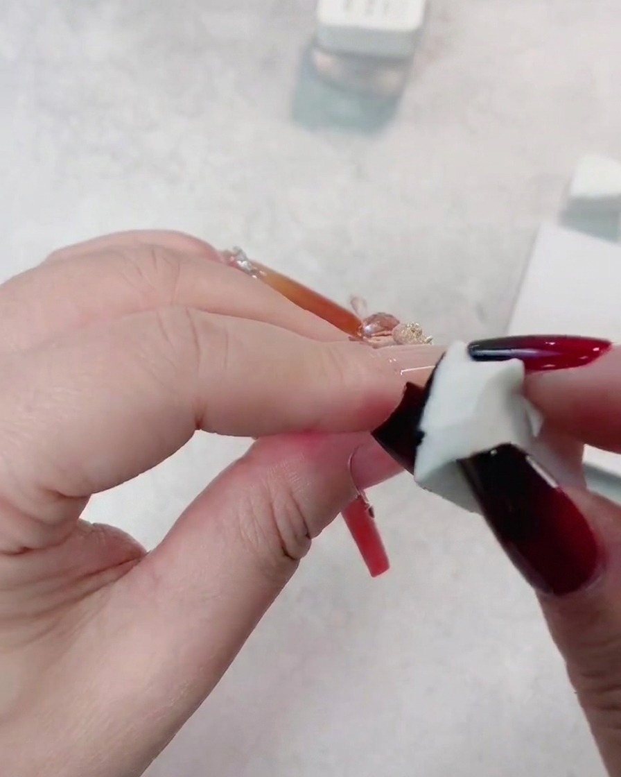 A sponge applying a second layer of black gel onto the tip of a dark red nail to deepen the gradient.