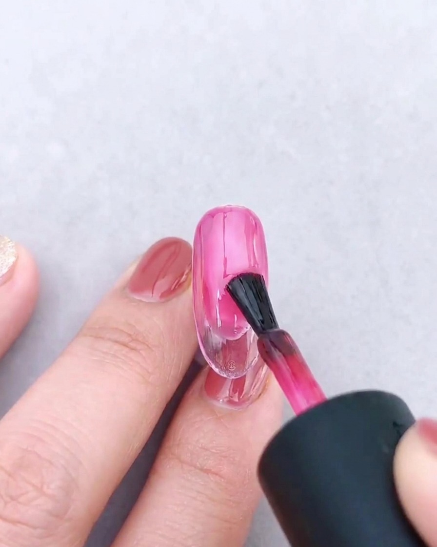 A nail brush applying a second coat of translucent pink gel over the existing gradient.