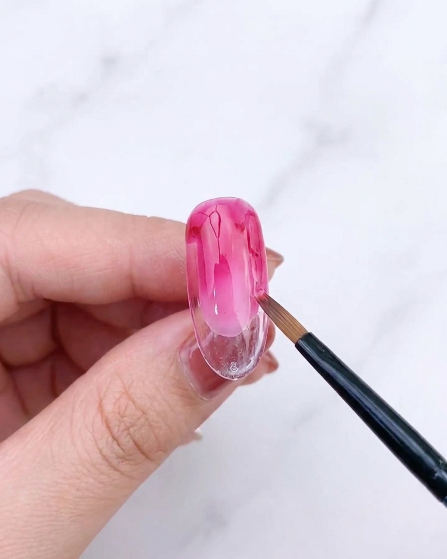 A fan brush blending the second layer of pink gel on a nail, creating a refined gradient.
