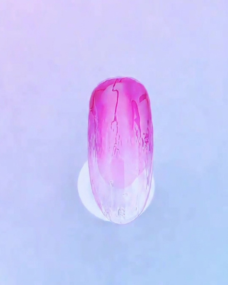A close-up of a nail brush applying a clear, even layer of base gel over the existing pink gradient nail design.