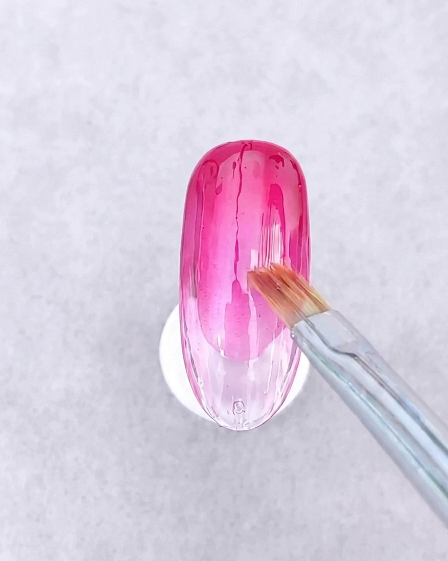 A pair of tweezers placing small, geometric pieces of glass paper and thin gold metal lines onto a wet gel surface.