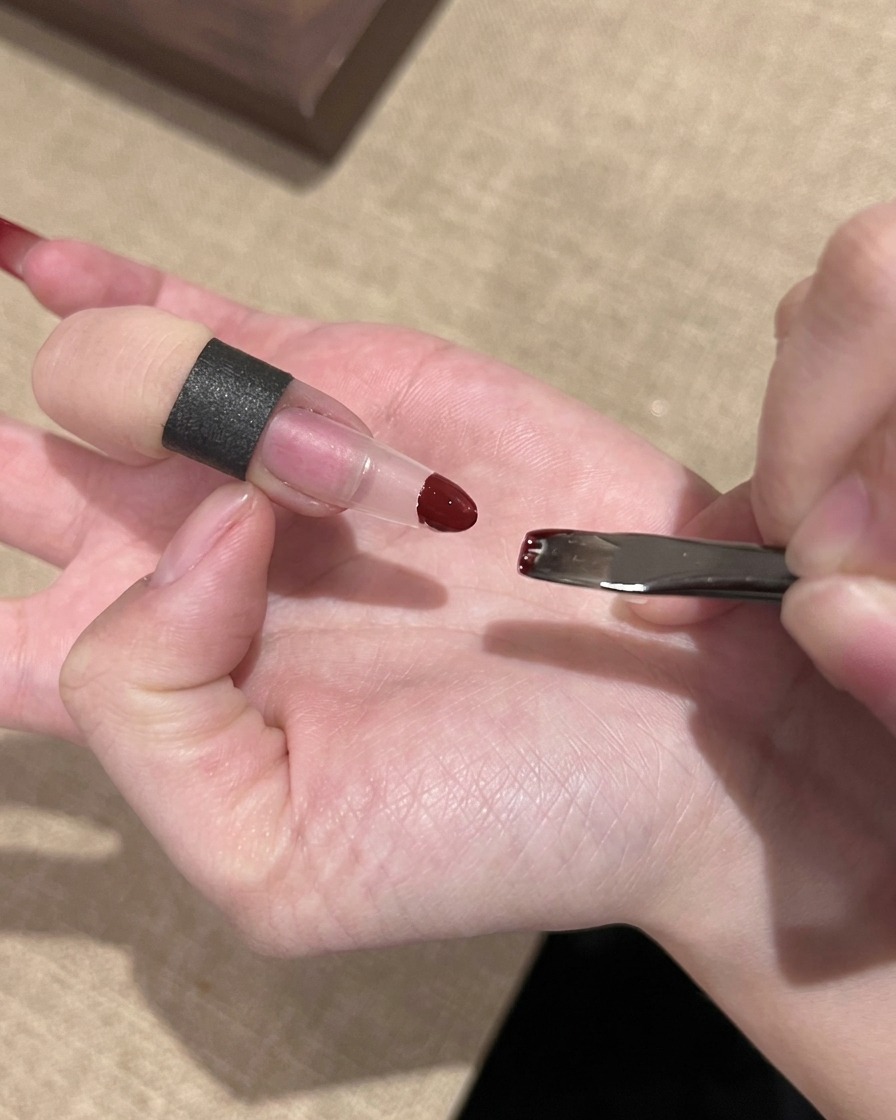 A hand using a small sponge to dab red gel polish onto the tip of a clear nail extension.
