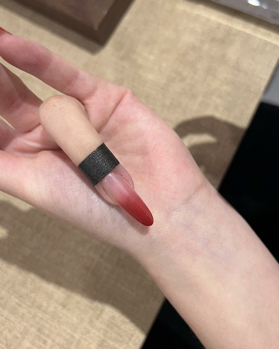 A single fingernail showing a cured red gradient effect transitioning from dark red to clear.