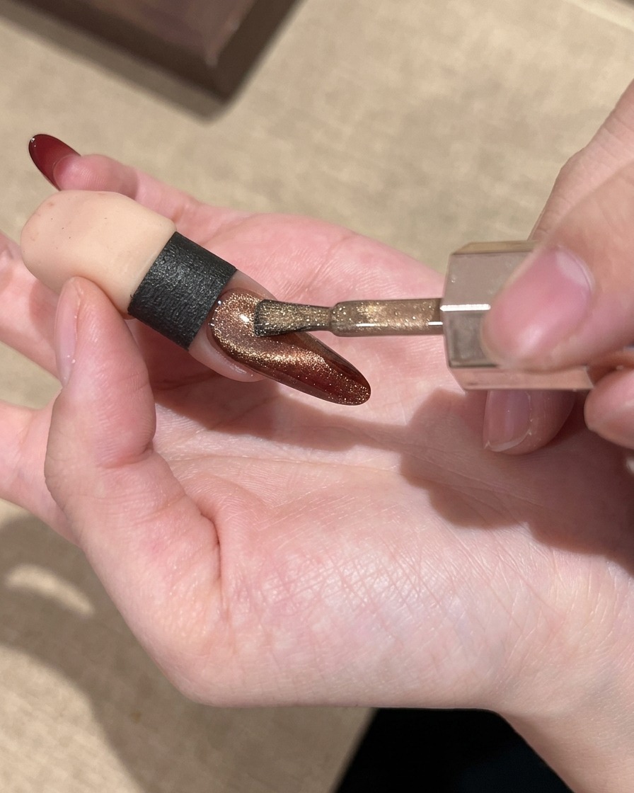 A nail brush applying a shimmering gold cat eye gel over the red gradient nail.